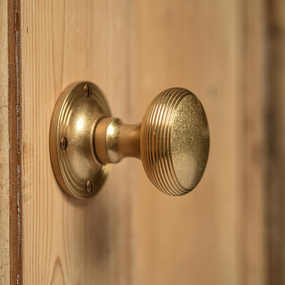 Aged Brass Reeded Cushion Door Knobs on a pine door