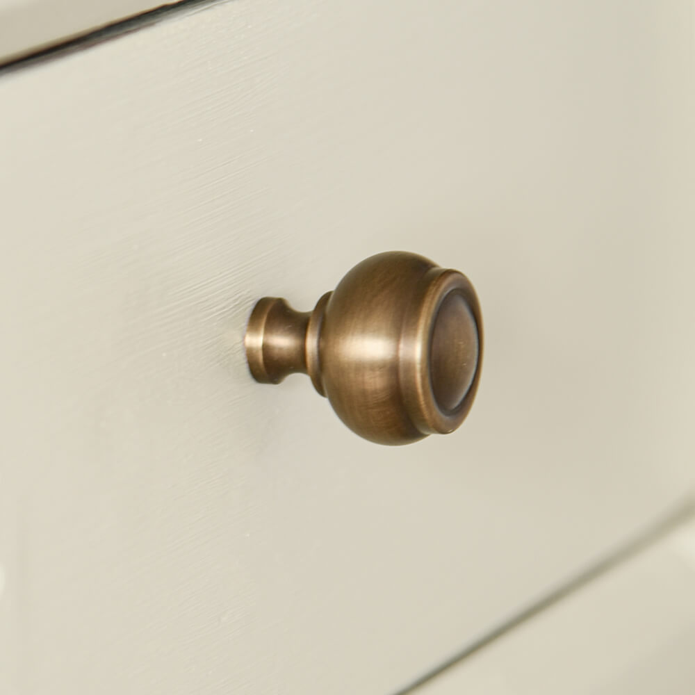 Rounded stepped cupboard knob design in antique brass on a cream drawer