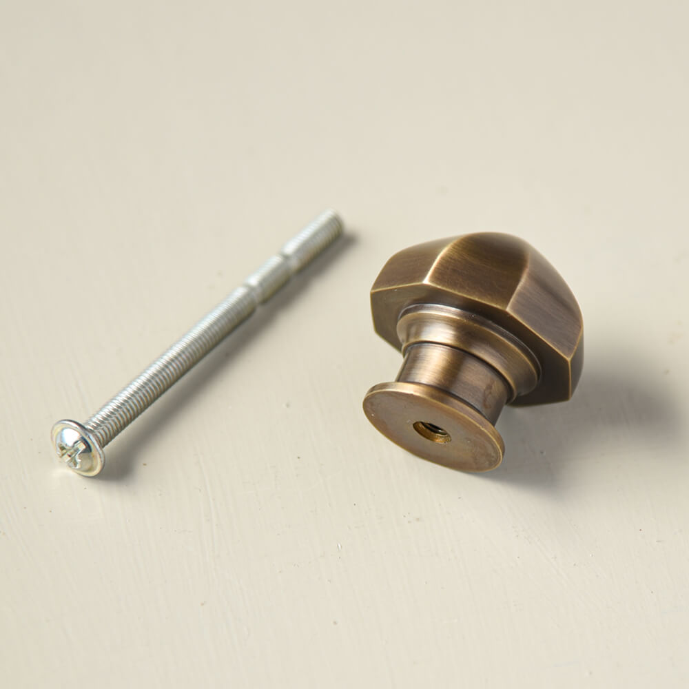 Pointy octagonal cupboard knob with a light antique brass finish shown with its fixing bolt