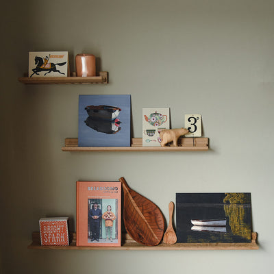 three oak picture shelves holding a variety of objects including books, paintings and candles