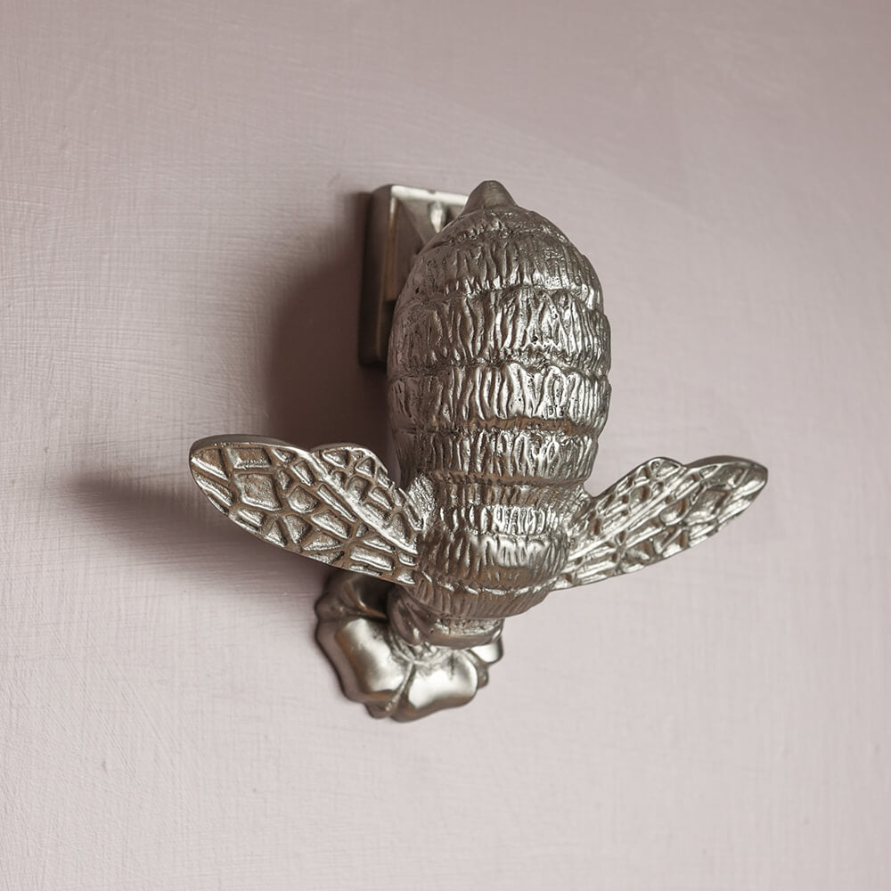 Silver bee door knocker with flower as strike plate on a pale lilac door