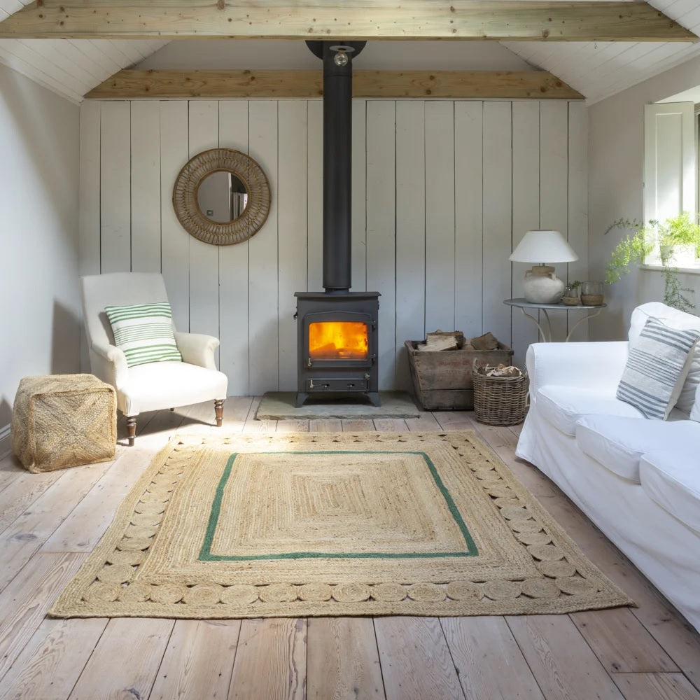 Rectangular jute rug with a rectangular green stripe in the centre on a wooden floor next to a white sofa and lit wood burner