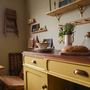 A kitchen with yellow cupboards and brass handles with various decorative features