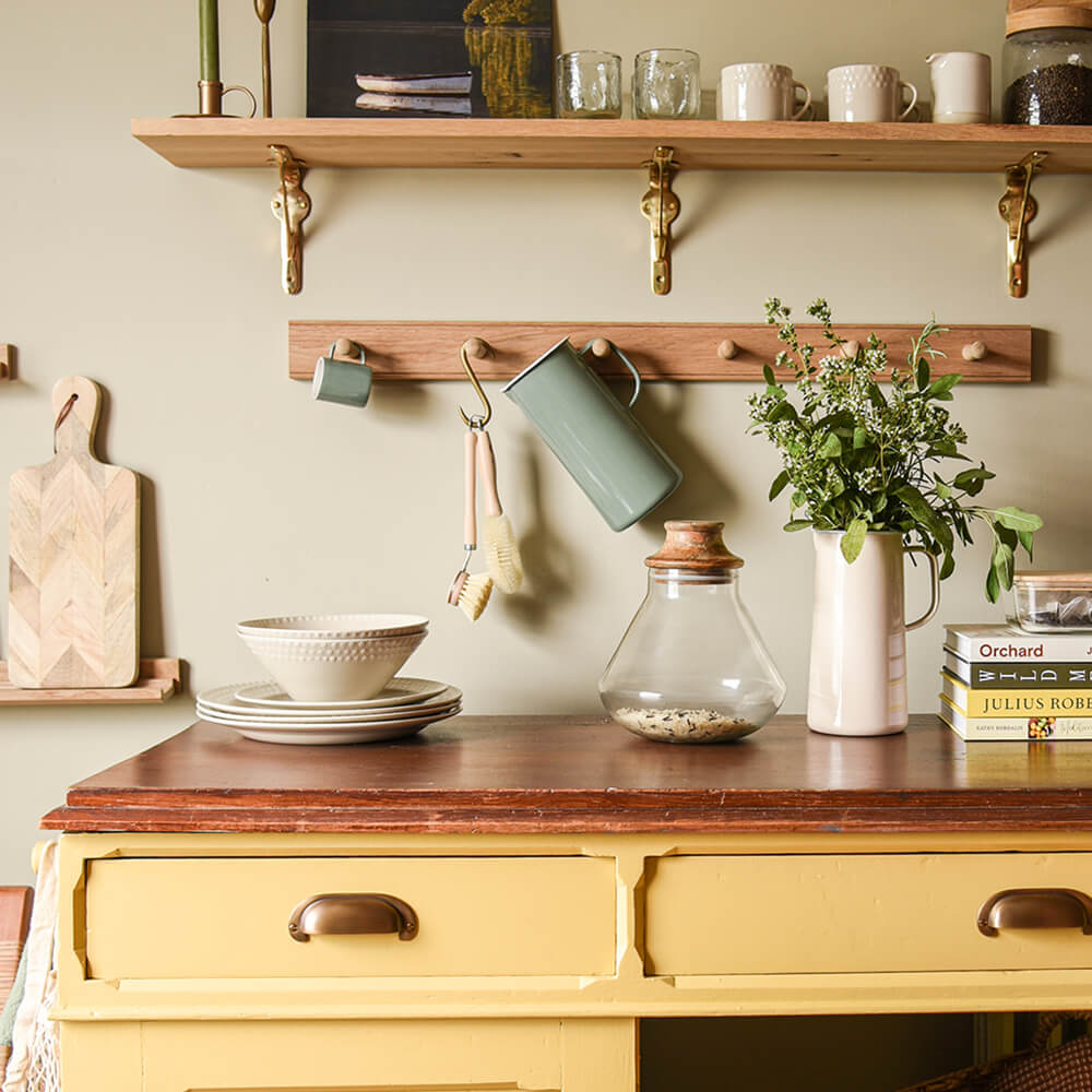 Yellow kitchen unit featuring curved brass handles 0n the drawers